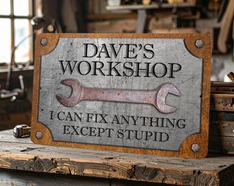 May include: A rectangular metal sign with a distressed silver finish and a rusted border. The text reads DAVE'S WORKSHOP and I CAN FIX ANYTHING EXCEPT STUPID. A large, rusted open-ended wrench is centered between the two lines of text.