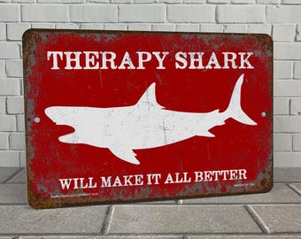 May include: A red metal sign with a white silhouette of a shark and the text "Therapy Shark Will Make It All Better".