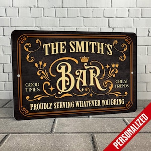 May include: A personalized wooden sign with a dark brown background and gold lettering. The sign reads "The Smith's Bar" with the words "Good Times" and "Great Friends" on either side of the bar name. The sign also says "Proudly Serving Whatever You Bring".