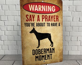May include: A warning sign with a red and white border that says "Warning Say a Prayer You're About to Have a Doberman Moment". The sign features a black silhouette of a Doberman Pinscher.