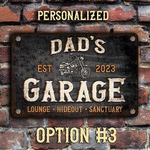 May include: A black metal sign with a distressed finish featuring the text "Dad's Garage Est. 2023 Lounge Hideout Sanctuary" with a motorcycle graphic.