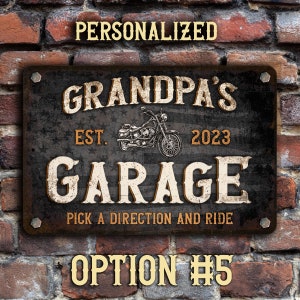 May include: A black metal sign with a distressed finish. The sign reads "Grandpa's Garage Est. 2023 Pick a Direction and Ride". A motorcycle is pictured in the center of the sign.