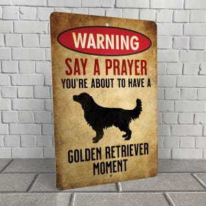 May include: A rustic metal sign with a warning message: "Warning Say a Prayer You're About to Have a Golden Retriever Moment". The sign features a silhouette of a Golden Retriever dog.