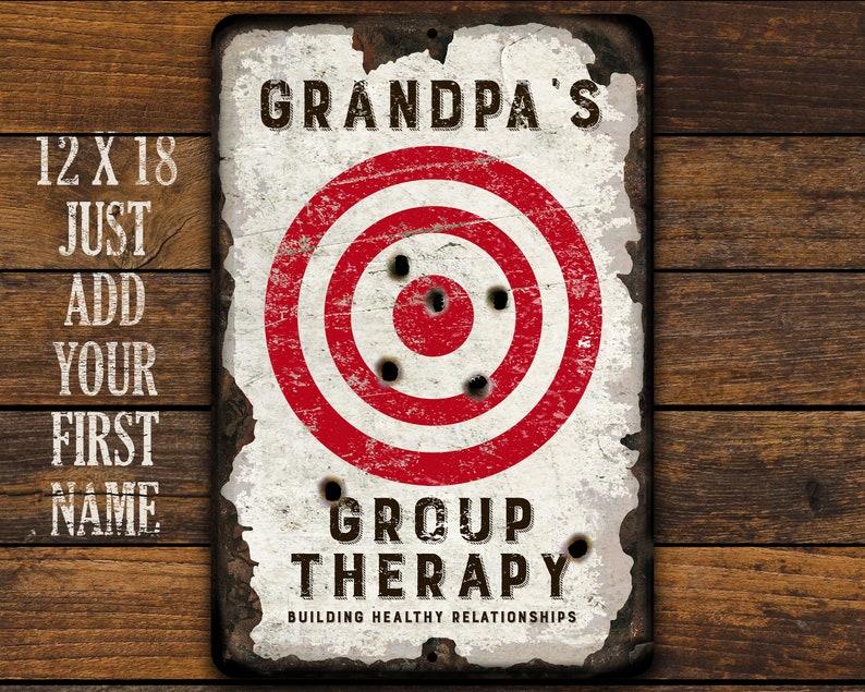 May include: A white metal sign with a red and white target in the center. The sign says "Grandpa's Group Therapy Building Healthy Relationships".