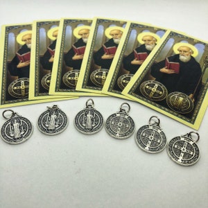 Puede incluir: Un conjunto de seis medallones de plata de San Antonio con una imagen en blanco y negro de San Antonio en un lado y una cruz con la inscripción "ND SM D" en el otro. Los medallones se muestran sobre una superficie blanca con seis tarjetas de oración amarillas que muestran una imagen de San Antonio.