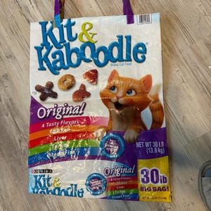 May include: A white ceramic mug with a black handle and the text "But First, Coffee" in a black, bold font. The mug is sitting on a wooden surface. The mug is approximately 4 inches tall.