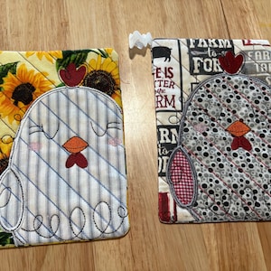 Puede incluir: Dos posavasos acolchados con diseños de pollos bordados. Un posavasos presenta un pollo blanco con rayas azules sobre un fondo amarillo con girasoles. El otro posavasos presenta un pollo gris con lunares negros sobre un fondo blanco con cuadros rojos y negros.