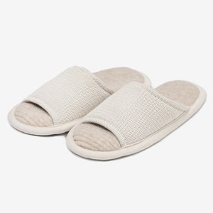 May include: A pair of beige open-toe slippers with a herringbone pattern on the top. The slippers have a soft, fuzzy lining.