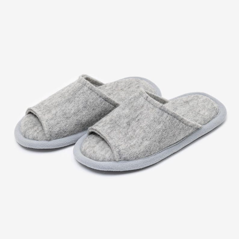 Peut inclure: Une paire de pantoufles en feutre gris avec un design &agrave; bout ouvert. Les pantoufles ont une semelle gris clair.