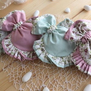 May include: Three fabric pouches with ruffled edges and floral patterns. The pouches are tied with a bow and are in shades of pink and blue.
