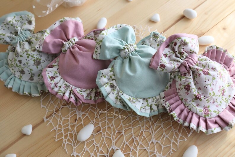 May include: Three fabric pouches with ruffled edges and floral patterns. The pouches are tied with a bow and are in shades of pink and blue.