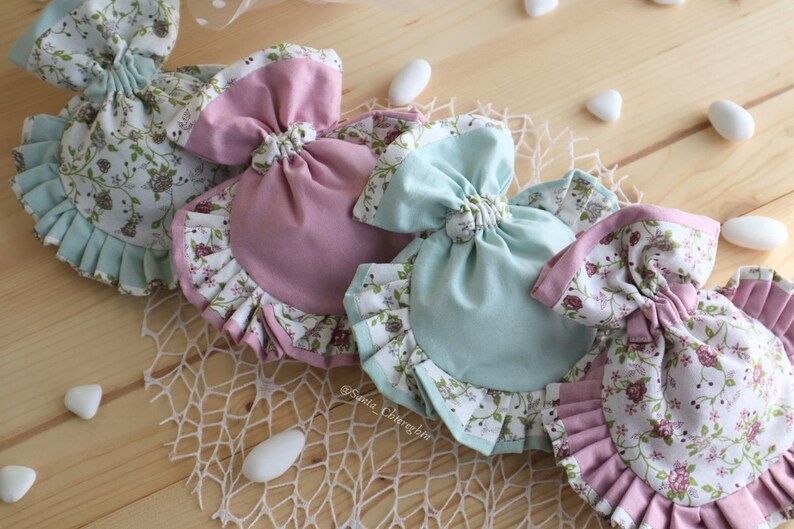 May include: Three fabric gift bags with floral print and ruffled edges. The bags are in shades of pink and blue and tied with a bow.