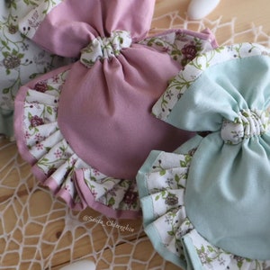 May include: Two fabric pouches with floral print and ruffled edges. One pouch is pink and the other is light blue. Both pouches are tied with a bow at the top.