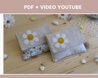 May include: Two small fabric pouches with a daisy design. The pouches are made of a light beige linen fabric with a white daisy embroidered on the front. The daisies have a yellow centre. The pouches are lined with a floral fabric.
