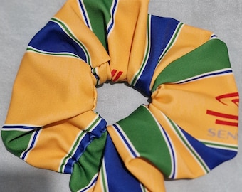 Peut inclure: Un chouchou avec un motif répété de rayures jaunes, vertes et bleues. Le chouchou porte l'inscription "SEN". Le tissu est froncé et élastiqué, créant un aspect froissé. Le chouchou est conçu pour maintenir les cheveux en place.