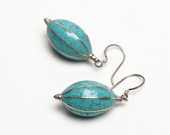 May include: A pair of turquoise blue earrings with silver wire detailing. The earrings are oval shaped and have a speckled texture.