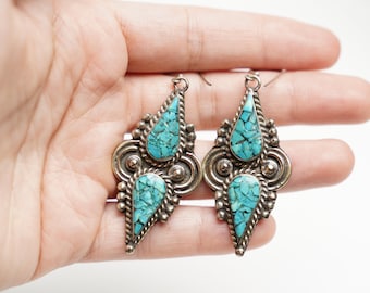 May include: A pair of silver dangle earrings with turquoise stones. The earrings are in the shape of a teardrop with a smaller teardrop stone at the bottom.