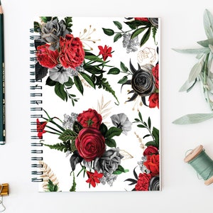 May include: A white spiral notebook with a floral pattern featuring red, black, and gray roses, leaves, and stems. The floral pattern is repeated throughout the notebook.