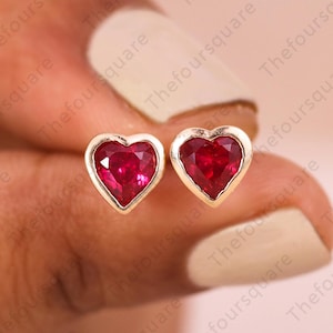 Pode incluir: Um par de brincos de ouro em forma de coração com pedras de rubi vermelho.