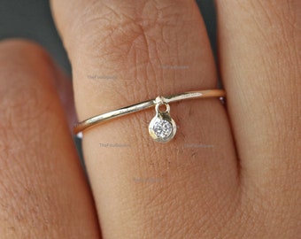 May include: A delicate gold ring with a small, round diamond dangling from the band.