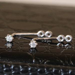 May include: Two silver nose rings with a small clear gemstone on each. The rings have a curved shape and are decorated with small circles.
