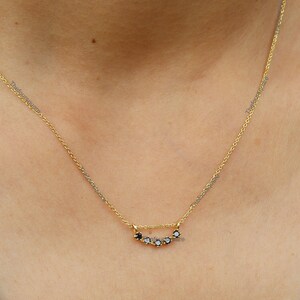 Op de afbeelding: Een gouden ketting met een delicaat hangertje met vijf kleine zwarte edelstenen in een gebogen lijn.