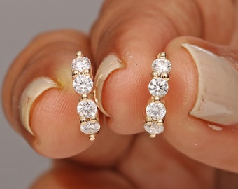 May include: A pair of gold hoop earrings with a row of three round clear cubic zirconia stones on each hoop.