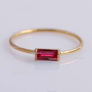 May include: A thin gold band ring with a single red rectangular gemstone.