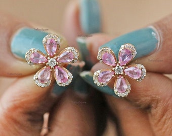 Puede incluir: Un par de pendientes de oro en forma de flor con piedras preciosas rosas y blancas.