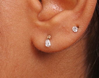 May include: Close-up of a person's ear with two small diamond earrings. The earring on the lower lobe is a teardrop shape, while the earring on the upper lobe is a round shape.