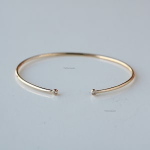 Op de afbeelding: Een delicate gouden armband met twee kleine, heldere edelstenen aan de uiteinden.