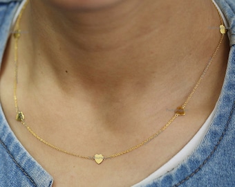 Op de afbeelding: Een delicate gouden ketting met kleine hartvormige hangers. De ketting wordt gedragen tegen een spijkerjasje, met de harten gelijkmatig verdeeld over de fijne ketting. Een eenvoudig maar elegant sieraad.