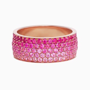 May include: A wide rose gold band ring with a gradient of pink sapphires. The ring is set with multiple rows of sapphires, creating a colorful and eye-catching design.