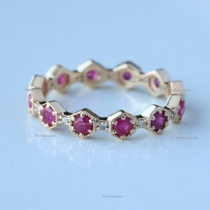 May include: A gold band ring with a repeating pattern of hexagonal settings. Each setting holds a round red ruby and a small round diamond.