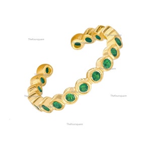 May include: Gold ring with a row of green gemstones. The ring is open and has a slightly curved shape.