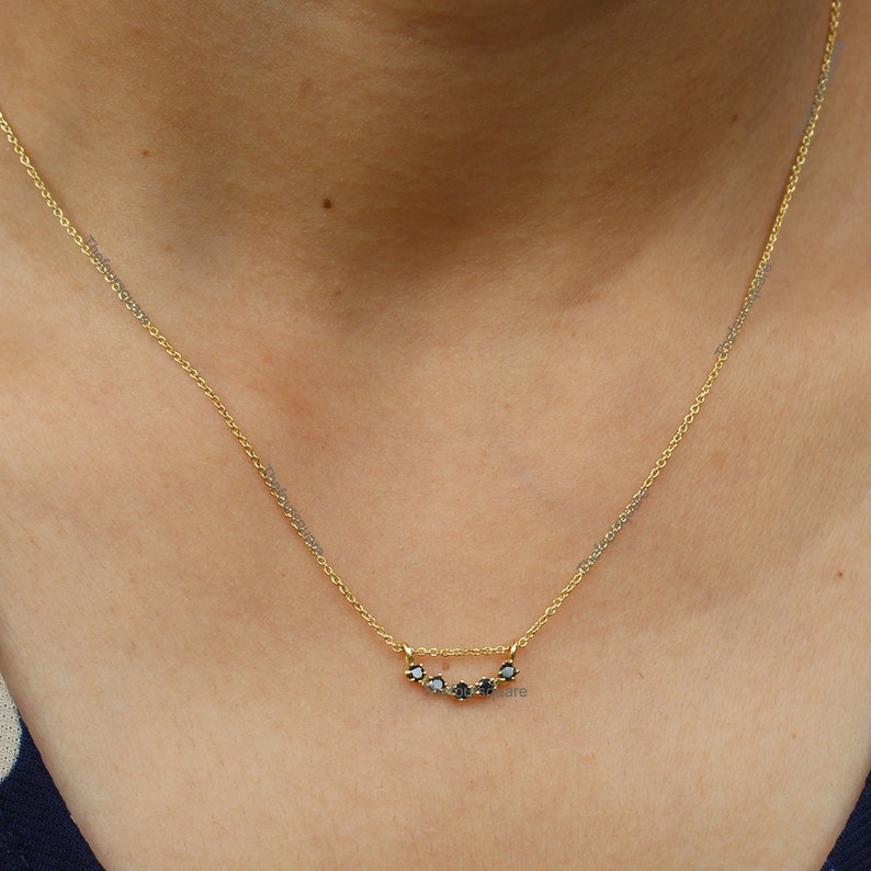 Op de afbeelding: Een gouden ketting met een delicate rij zwarte diamanten in een gebogen vorm.