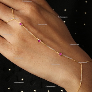 May include: A gold chain bracelet with three pink gemstones. The bracelet is designed to be worn around the wrist and up the hand, with the chain extending to the finger.