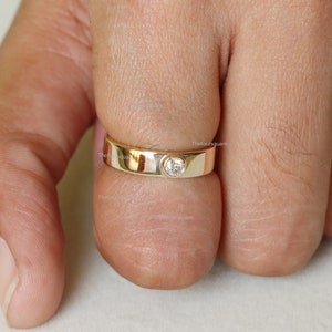 Puede incluir: Un anillo de banda de oro con un solo diamante redondo engastado en el centro.