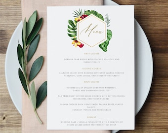May include: A white menu card with gold text and a floral design, featuring a tropical theme. The menu includes a list of courses for a wedding. The card is placed on a white plate with a pink napkin and greenery.