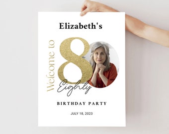May include: A white poster with the text "Welcome to Eighty" in gold glitter lettering. The number 8 is large and the text "Eighty" is in cursive. The poster also includes the text "Elizabeth's Birthday Party" and "July 18, 2023". A photo of a woman is in the center of the poster.