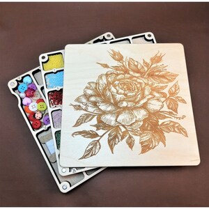 May include: A wooden box with a hinged lid, featuring a laser-engraved design of a rose with leaves. The box has multiple compartments for storing small items, such as beads, buttons, or other craft supplies.