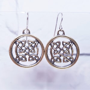 May include: A pair of silver dangle earrings with a gold Celtic knot design. The knots are in a circular shape and are open in the center.