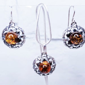 Peut inclure: Un collier et des boucles d'oreilles en argent avec des pierres d'ambre. Le collier et les boucles d'oreilles présentent un design délicat et orné.