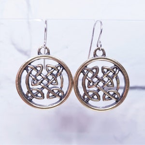 May include: A pair of silver dangle earrings with a gold Celtic knot design. The knots are intricate and detailed, and the earrings are a beautiful example of Celtic jewelry.
