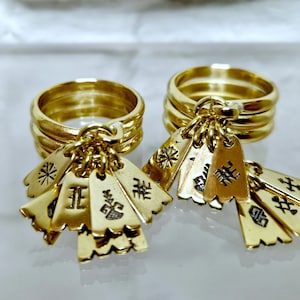 May include: Two gold rings with multiple charms hanging from them. The charms are shaped like small rectangular tags with different symbols and characters engraved on them.