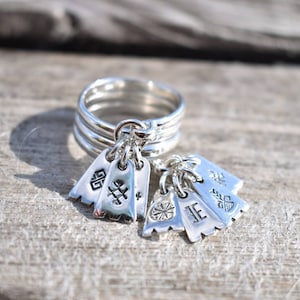 May include: A silver ring with multiple charms hanging from it. The charms are shaped like small flags and have different symbols engraved on them.