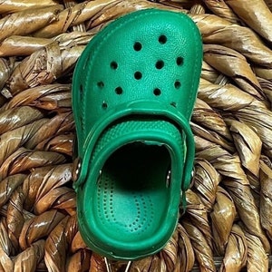 May include: A green rubber clog with a textured surface and a strap across the top. The clog has a round toe and a small heel.