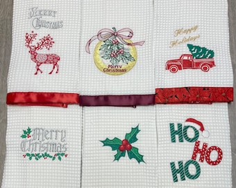 Puede incluir: Conjunto de seis toallas de cocina blancas de tejido de gofre con diseños navideños bordados en rojo, verde y dorado. Los diseños incluyen un reno, un árbol de Navidad, una rama de acebo, una corona y las palabras "Feliz Navidad" y "Ho Ho Ho".