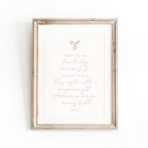 May include: A framed print with a pink ribbon at the top and the text "Now I lay me down to sleep I pray the Lord my soul to keep May angels watch me through the night And wake me with the morning light Amen."
