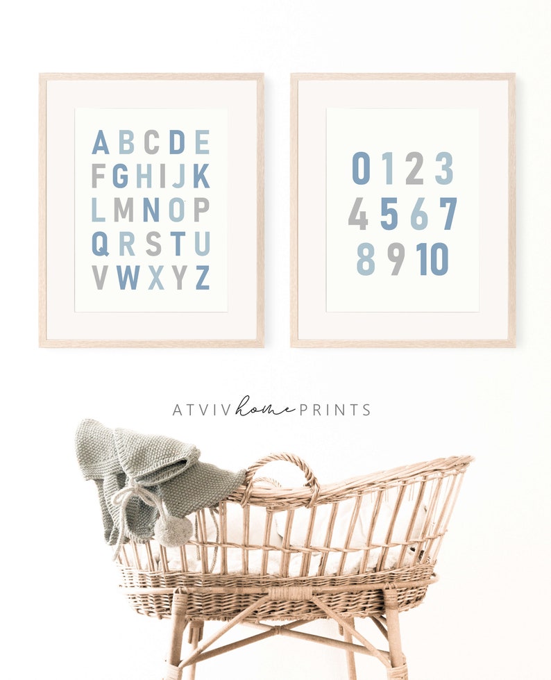 May include: Two framed prints with a white background and blue and gray letters and numbers. The print on the left has the alphabet in blue and gray letters. The print on the right has the numbers 0-10 in blue and gray numbers. The prints are hanging on a white wall above a wicker bassinet.